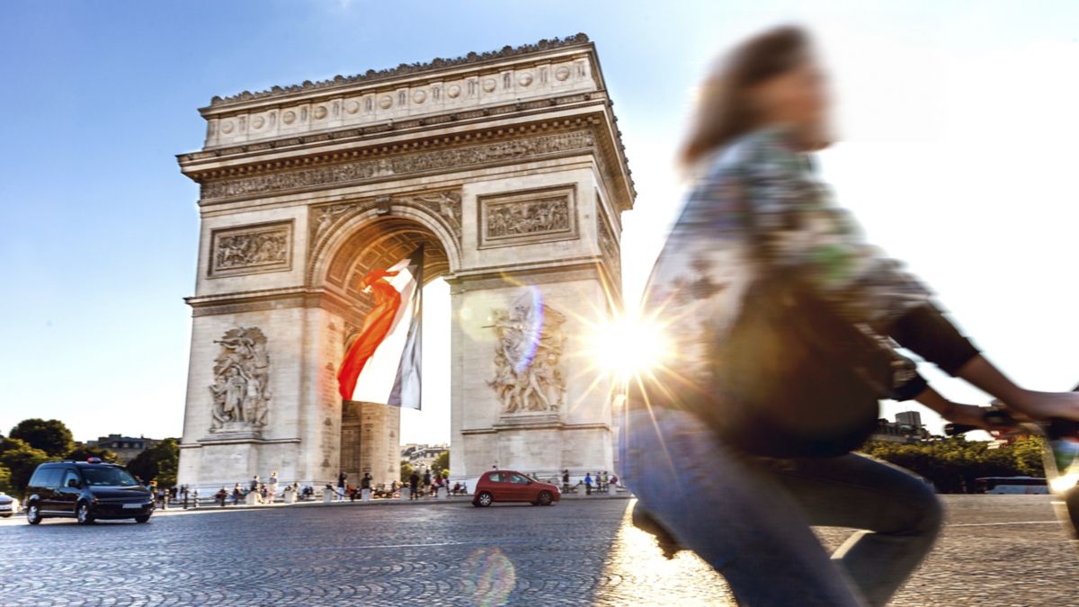 Adult cycling past Arc de Triomphe in Paris.