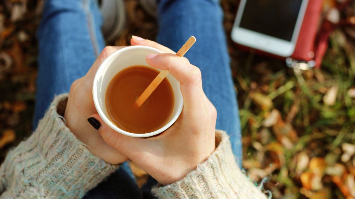A low view of a person holding a cup of tea on an Autumn day in the park in London.