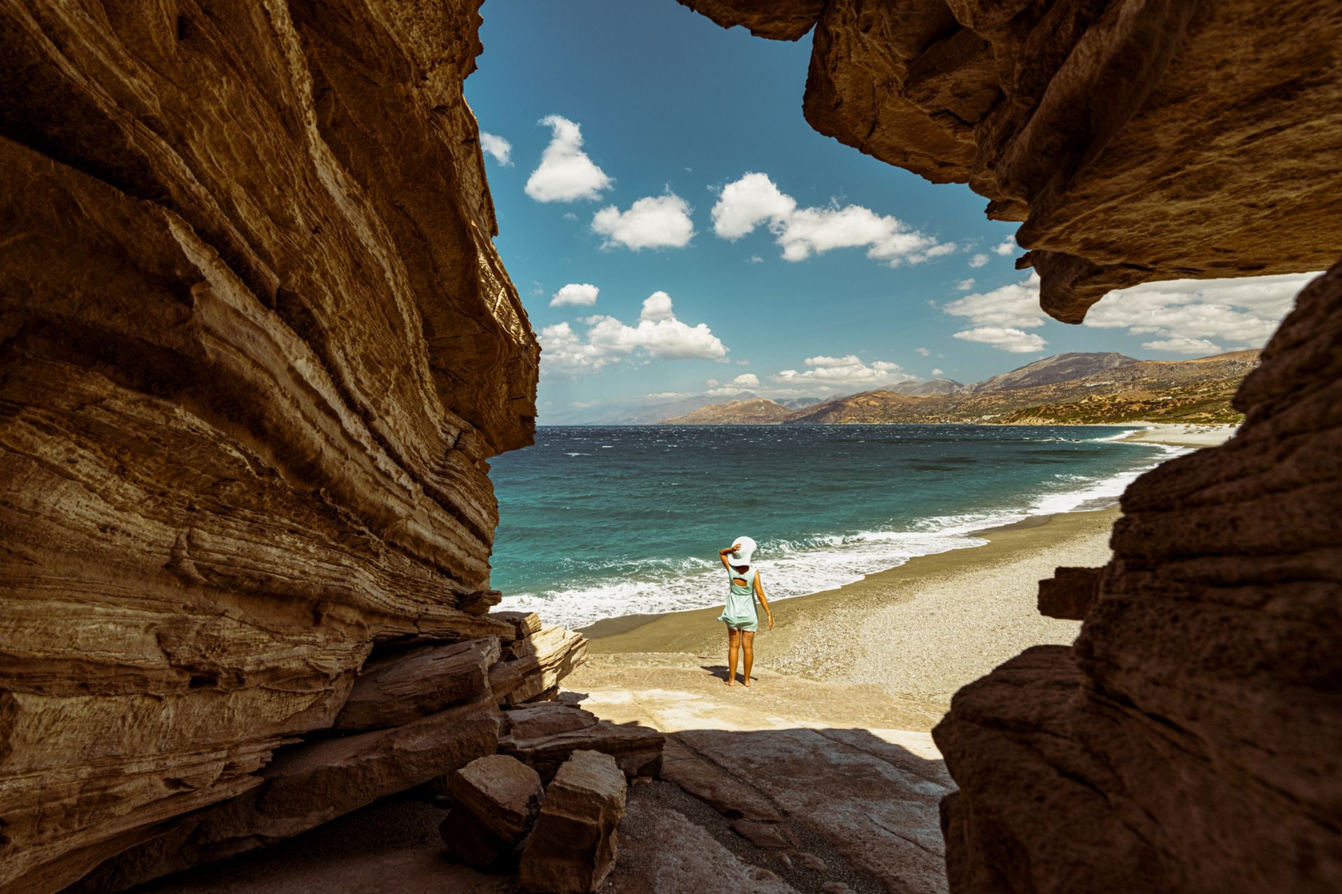 Adult wearing sun hat looking out to sea near a cave on Triopetra beach, Plakias, Crete, Greece.