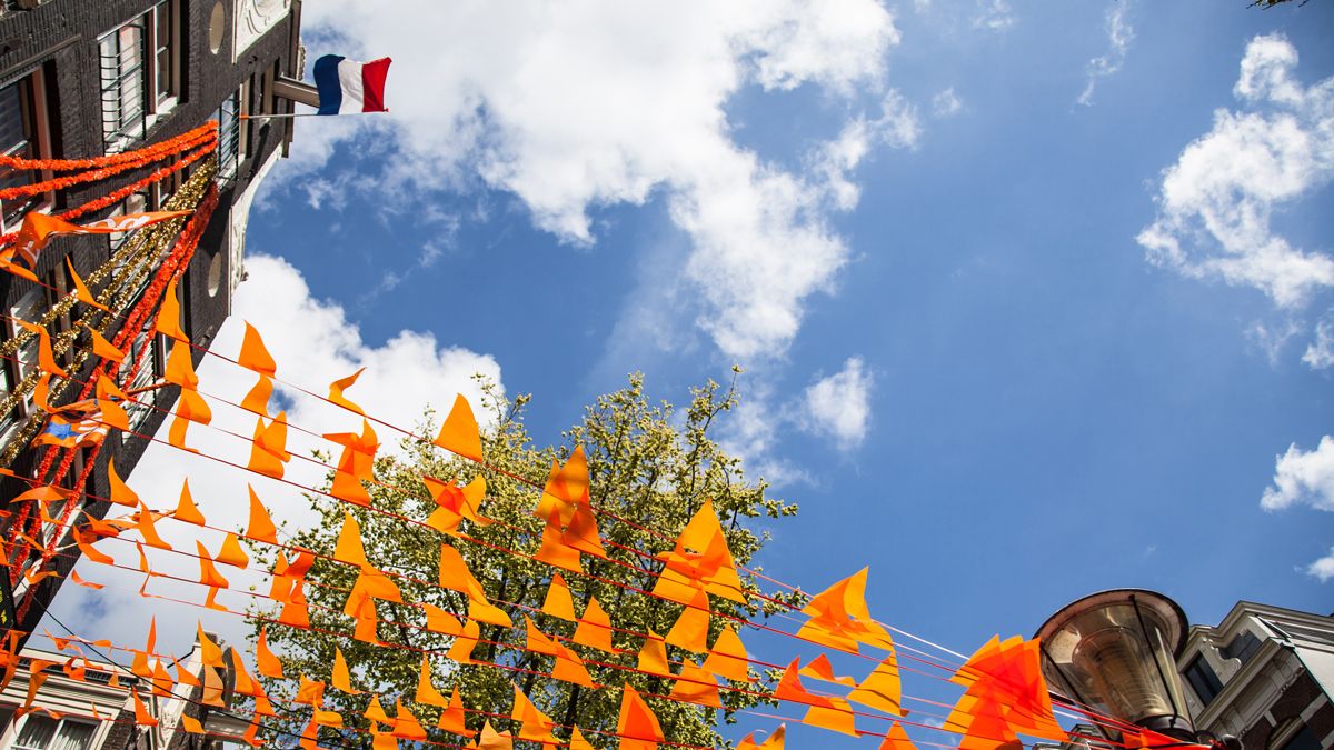 Orange bunting hanging above the streets of Amsterdam for King’s Day, linking to BA High Life website.