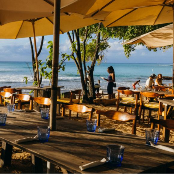 People enjoying drinks and views from a beach bar in Barbados, linking to BA High Life site.