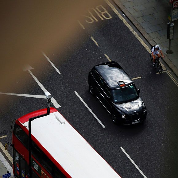 Aerial view of a black cab making its way through London alongside a London bus and cyclist, linking to BA High Life site.​