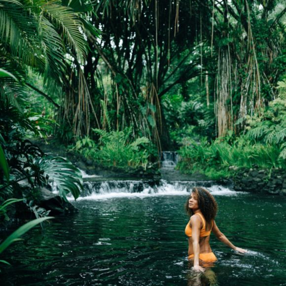 A woman in an orange swimsuit enjoying a dip in a natural pool, linking to BA High Life website.