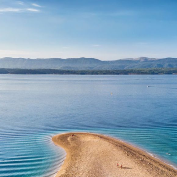 A narrow, curved sandy spit extending into calm blue water in Croatia, linking to BA High Life site.