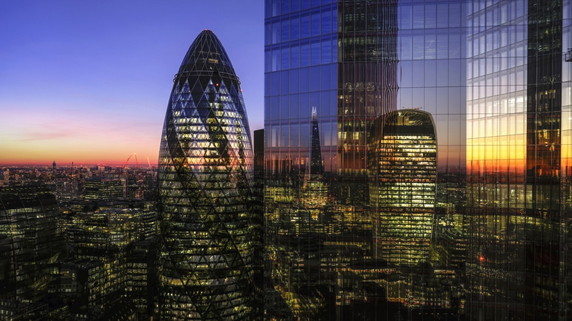 Modern skyscrapers in the financial district of London viewed from high up, illuminated at dusk.
