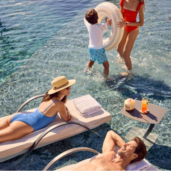 Children play in the water while a couple relax on loungers at Hilton Cancun, linking to BA High Life site.​