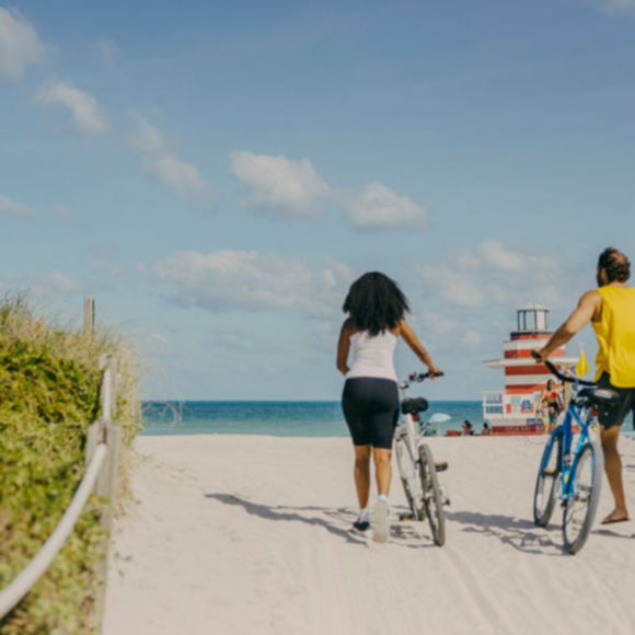 Two people walking with bikes on Miami Beach, linking to www.bahighlife.com.