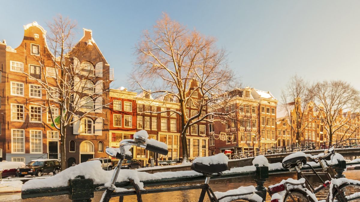 Bicycles covered with snow alongside canal during winter in Amsterdam.