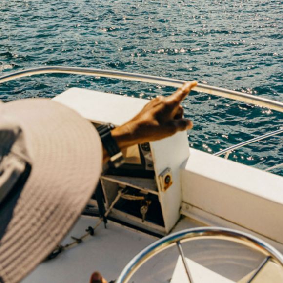A traveller in a hat points into the distance while driving a boat through the waters of St Lucia, linking to BA High Life site.