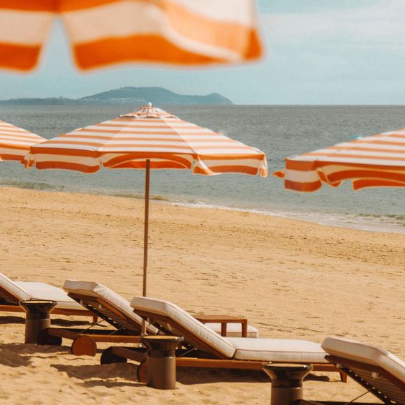 Loungers under striped umbrellas on a beach in Tamuda Bay, Morocco, linking to BA High Life website.