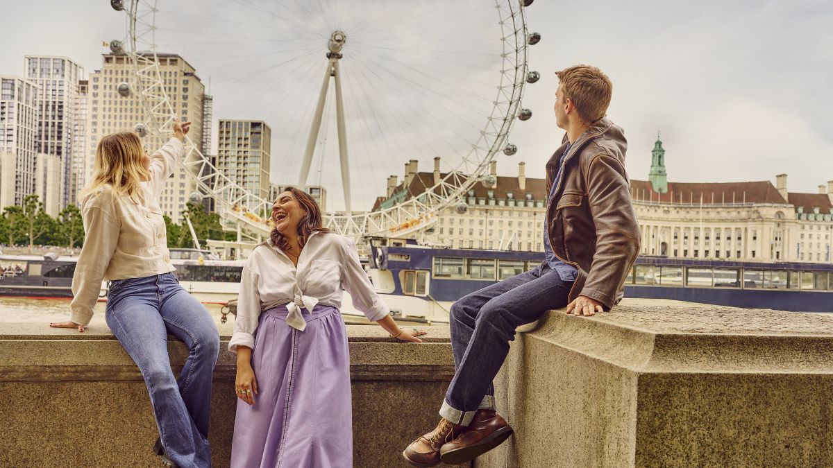 Three adult friends sitting by the London Eye.