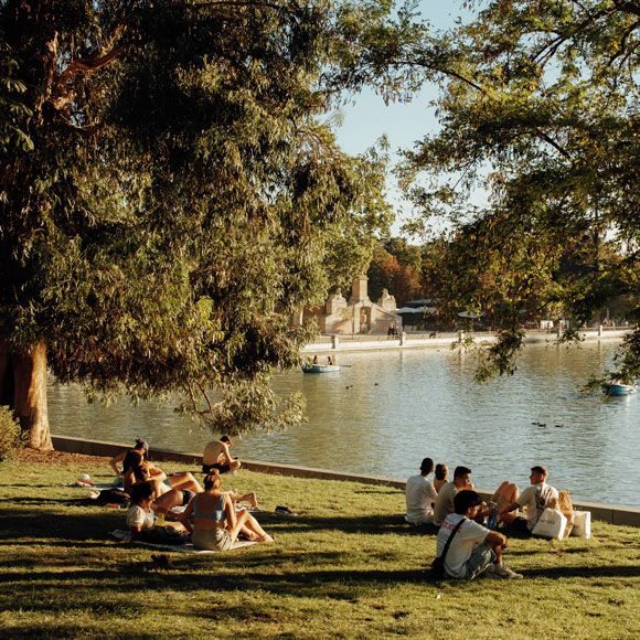 People sitting on the grass along the water’s edge in Madrid’s Retiro Park, linking to BA High Life site.
