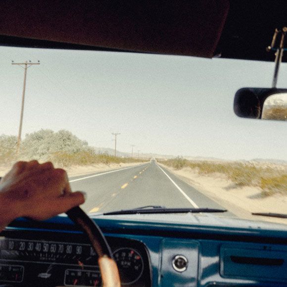 A driver's hand on the steering wheel and long road stretching into a desert landscape, linking to BA High Life site. 